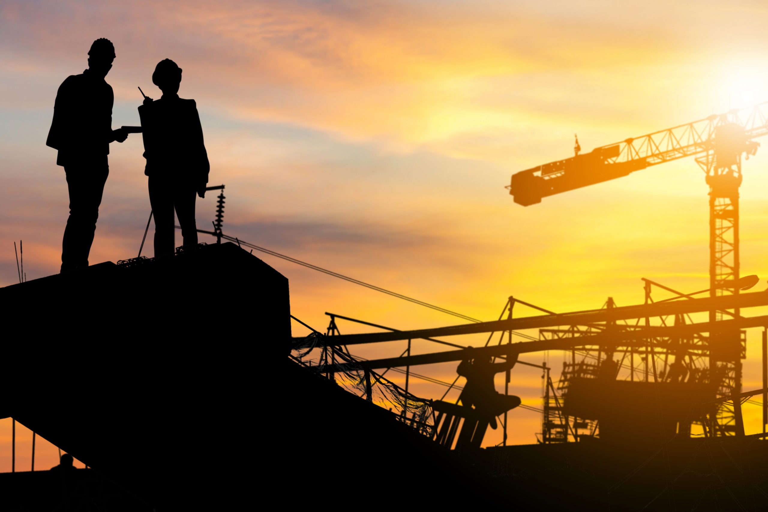 Silhouette of Engineer and worker checking project at building site background, construction site at sunset in evening time.